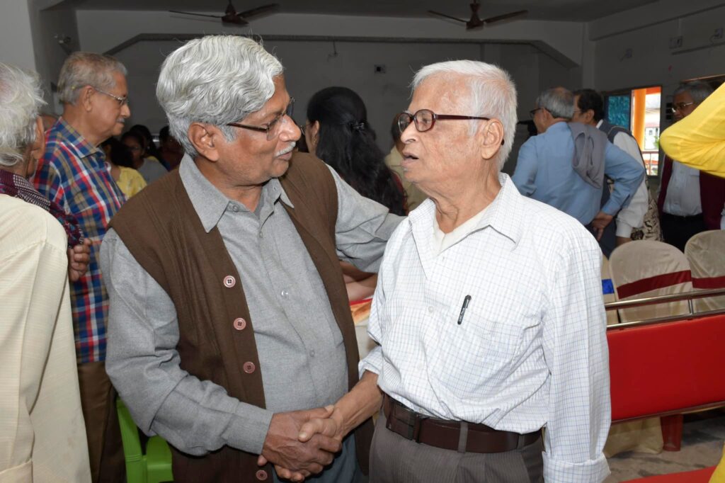 Two elderly guests shake hands and talk in the hall before the book launch begins.