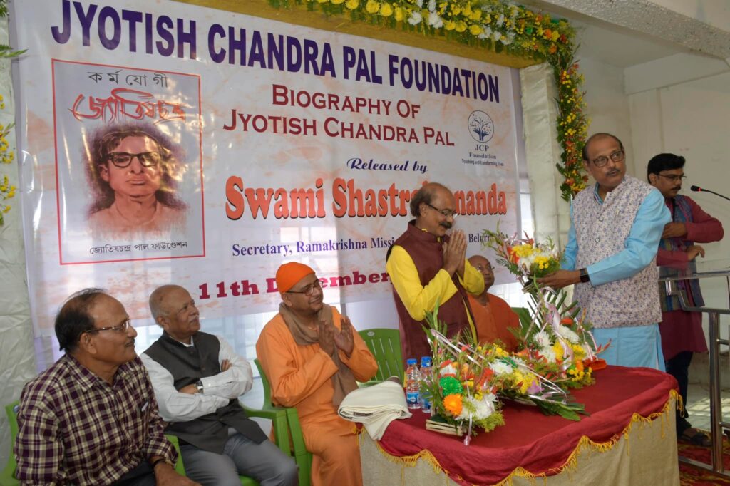 Dignitaries seated in front of the launch banner as one of them, hands folded in greeting, is presented with a bouquet.