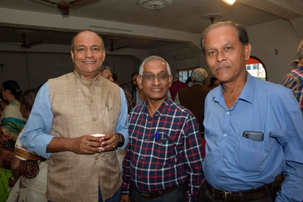 Three guests pose together in the hall, one of them holding a cup of tea.