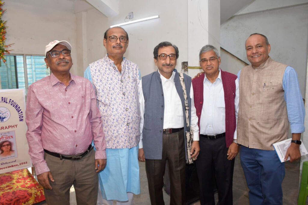 Five guests pose together beside the launch banner, one of them holding a copy of the biography.