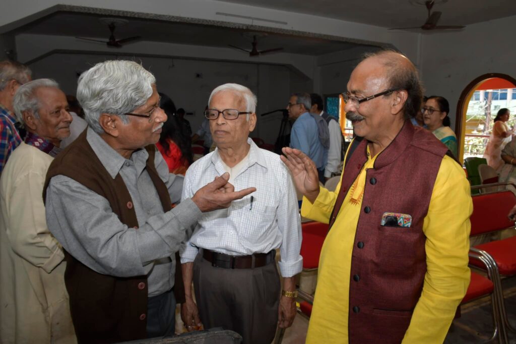 Three guests stand talking in the hall, one of them gesturing mid-conversation.