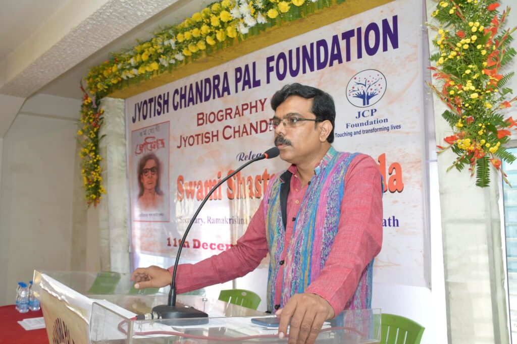 A speaker in a striped waistcoat addresses the audience from the podium at the book launch.