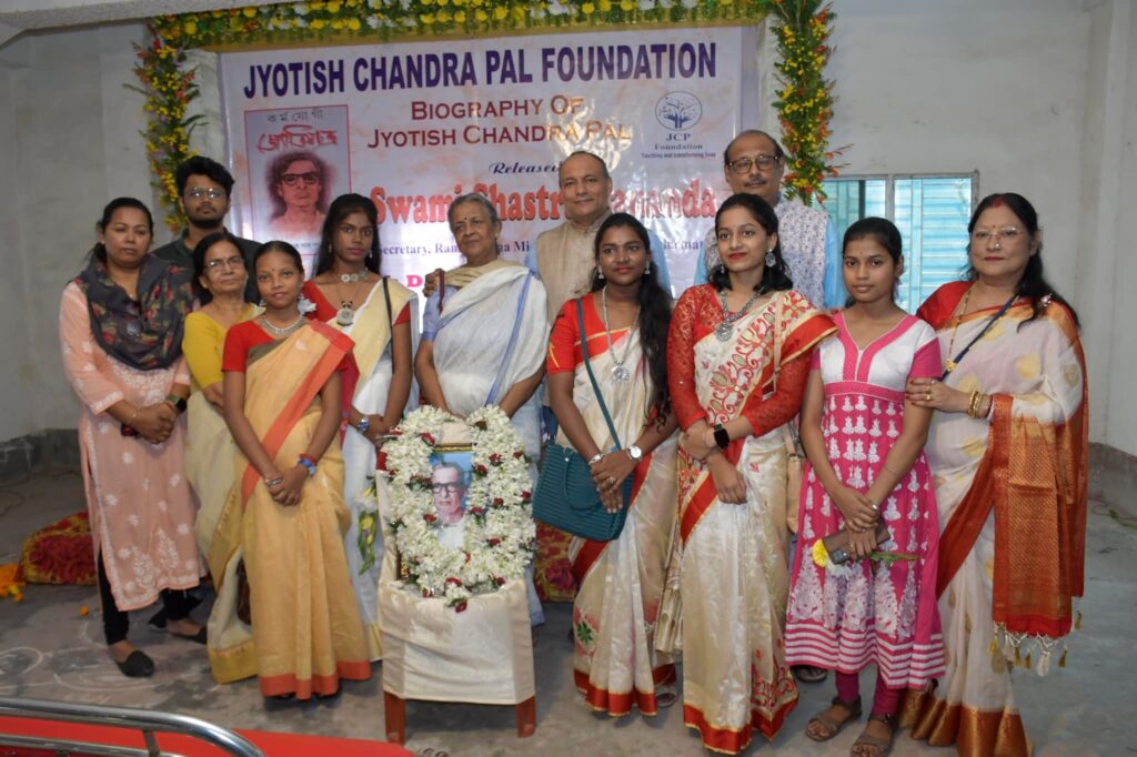 Twelve women, students and guests stand together behind the garlanded portrait of Jyotish Chandra Pal.